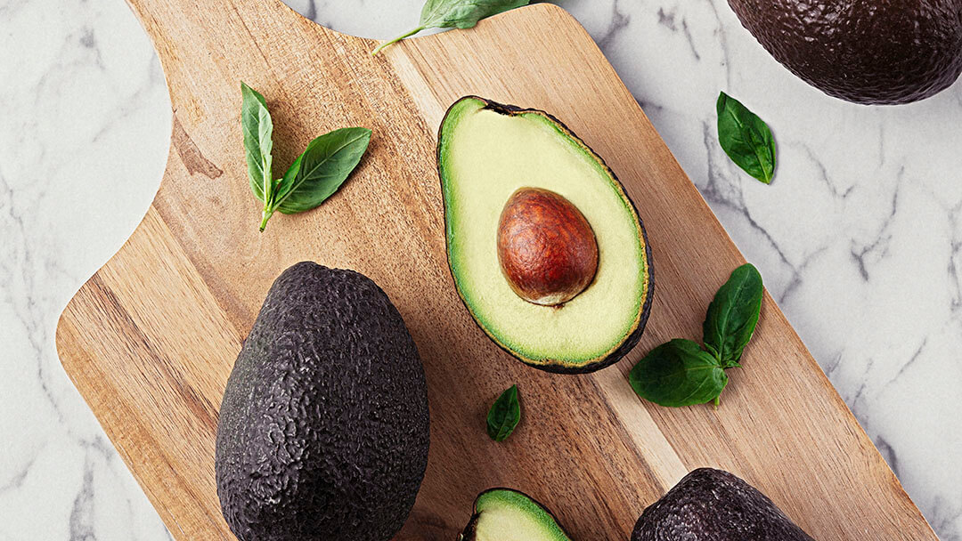 Wooden table with avocados and basil on marble stone