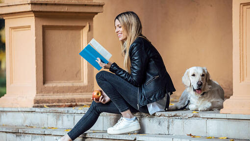 Woman reading a book with her lovely golden retriever dog in the park in autumn